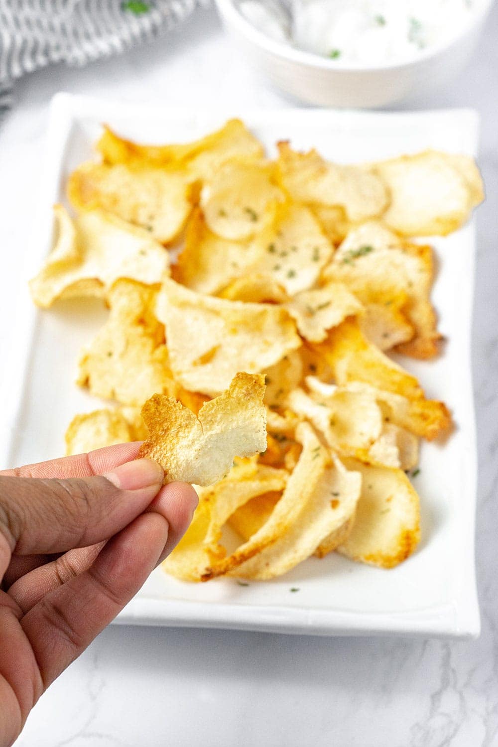 holding crispy jicama chips over a platter of chips on a white plate