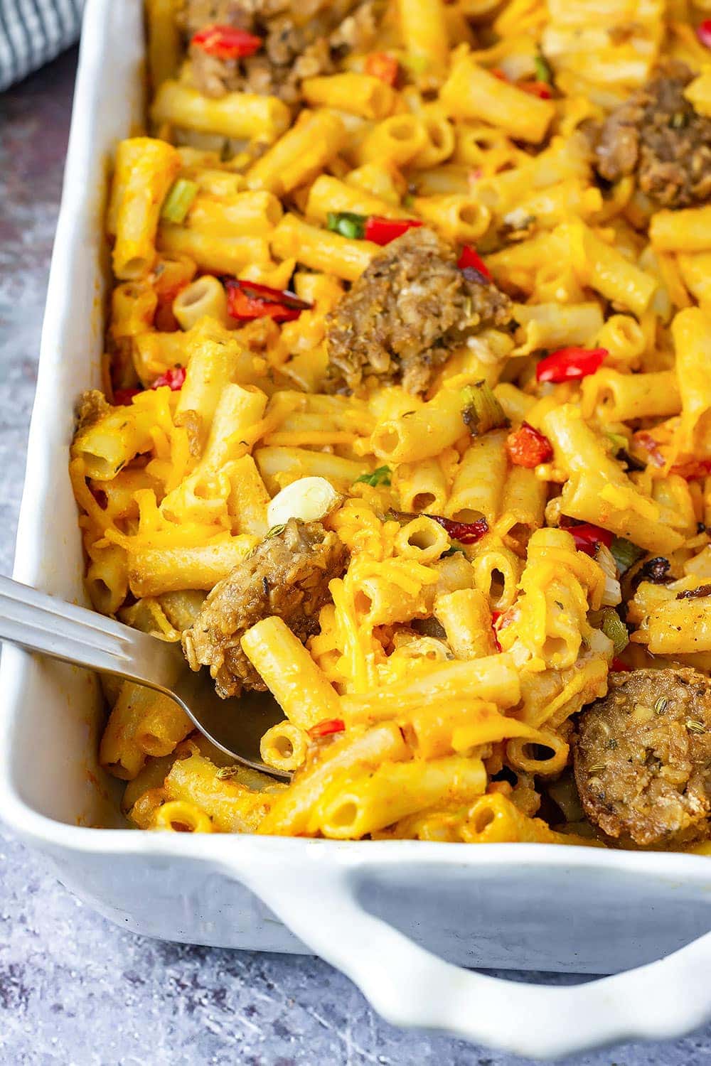 Cajun vegan baked mac and cheese in a white casserole pan, silver spoon serving
