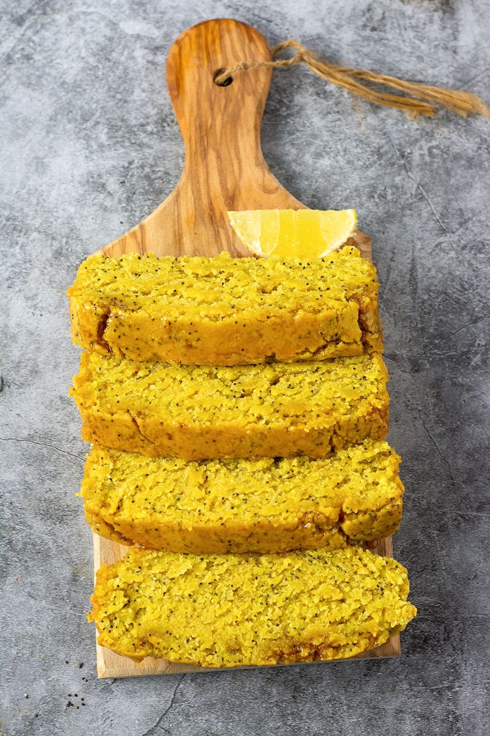 Overlay Lemon Poppy Seed Bread Vegan Gluten-free on a cutting board with lemon slices on a grey background