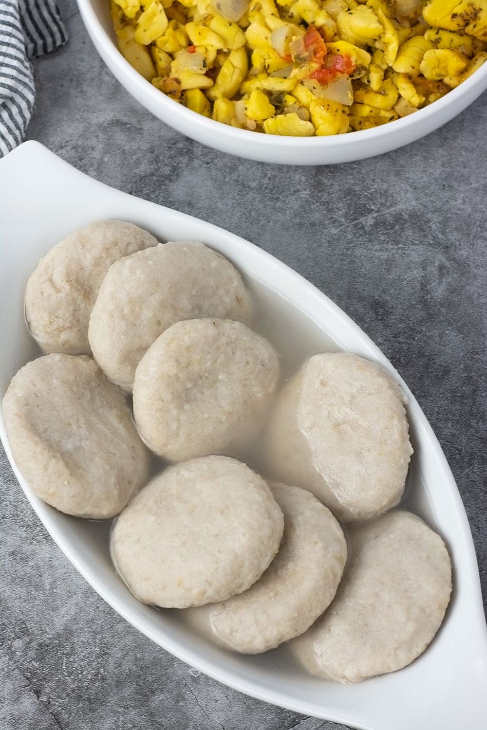 Green banana dumplings in a white casserole dish with vegan ackee in the background in a white bowl.