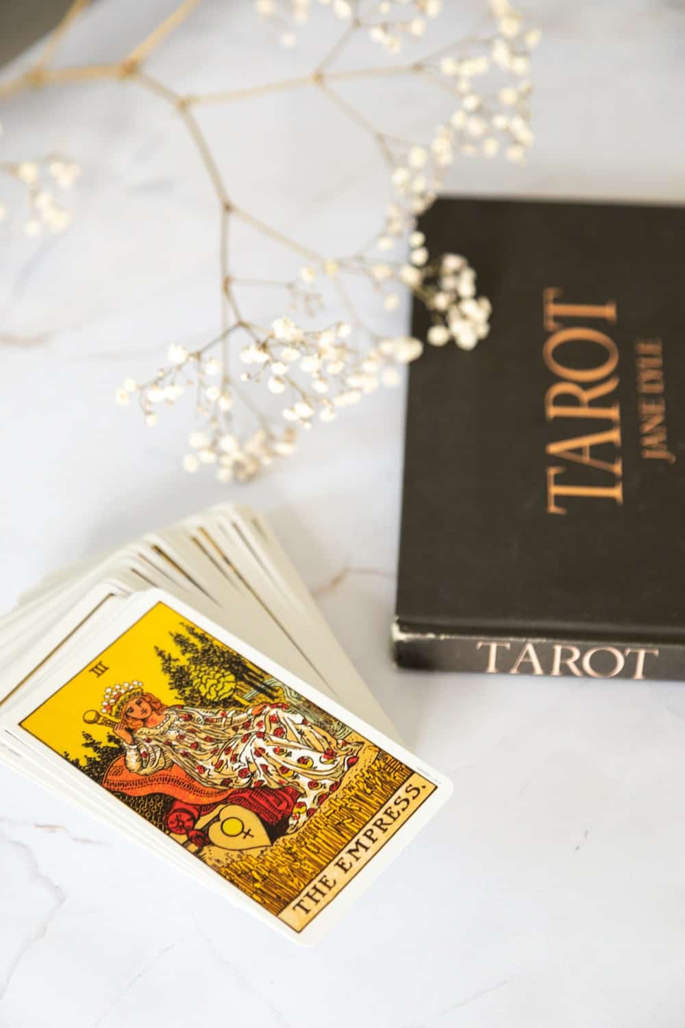 pile of tarot cards with the empress tarot card on top, placed on a white table next to a tarot book