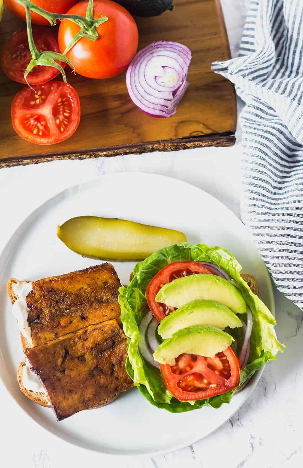 an open blt sandwich on a white plate with a pickle