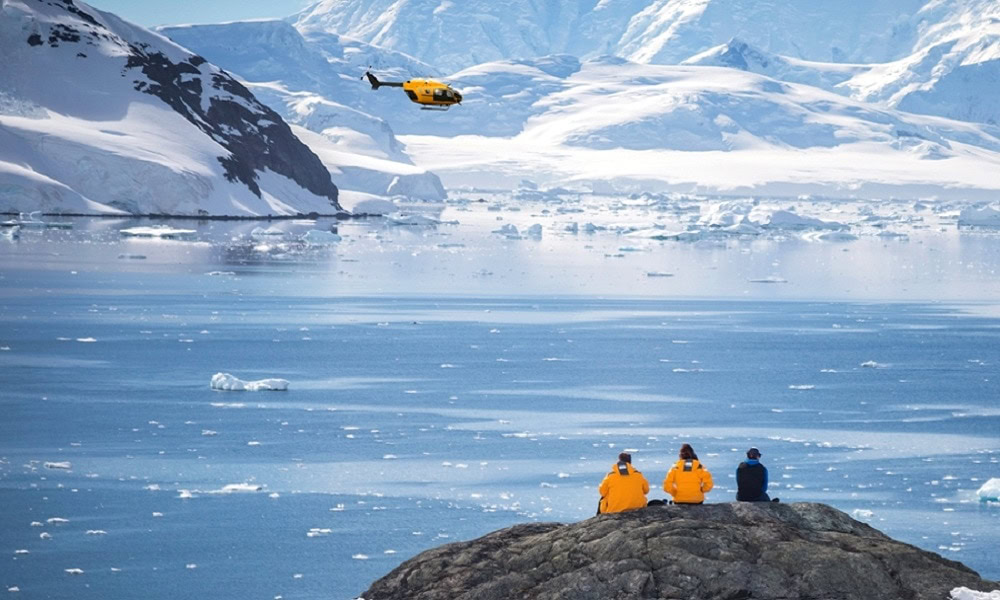 people sat on rock overlooking lake with helicopter on the horizon