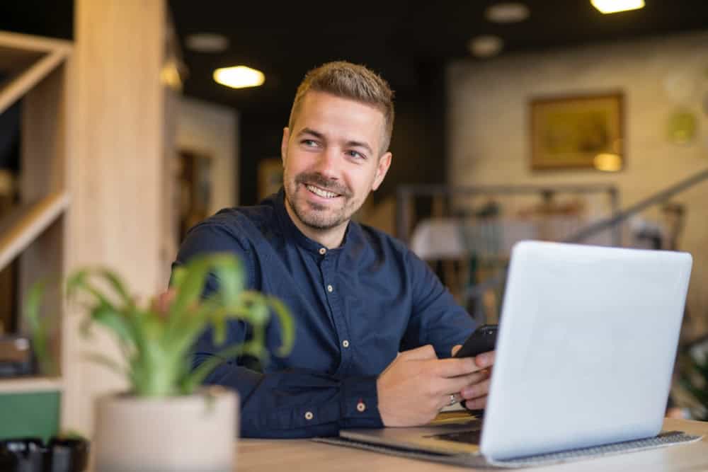 Male Entrepreneur Using Laptop & Phone Sitting At His Desk