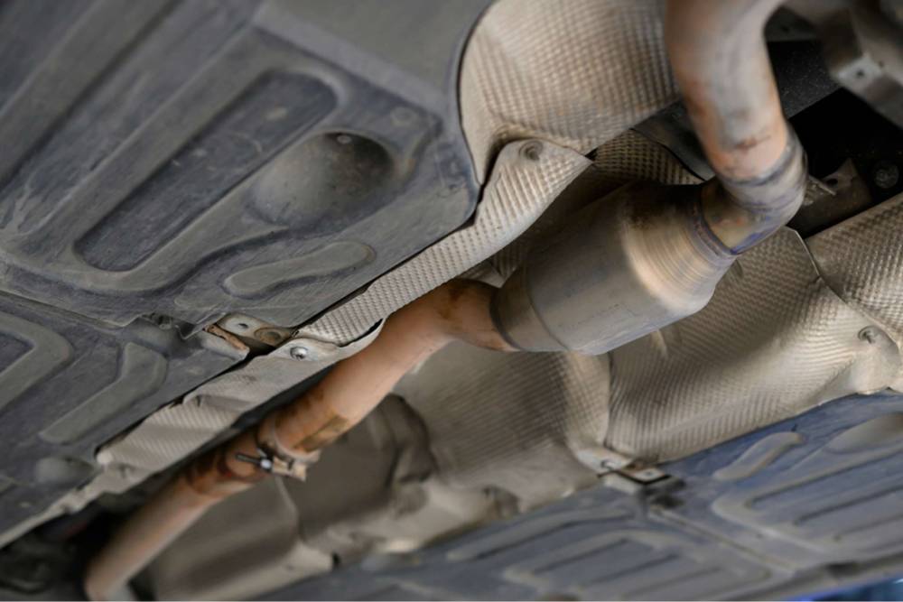 Mechanic replacing stolen catalytic converter under car at roadside service