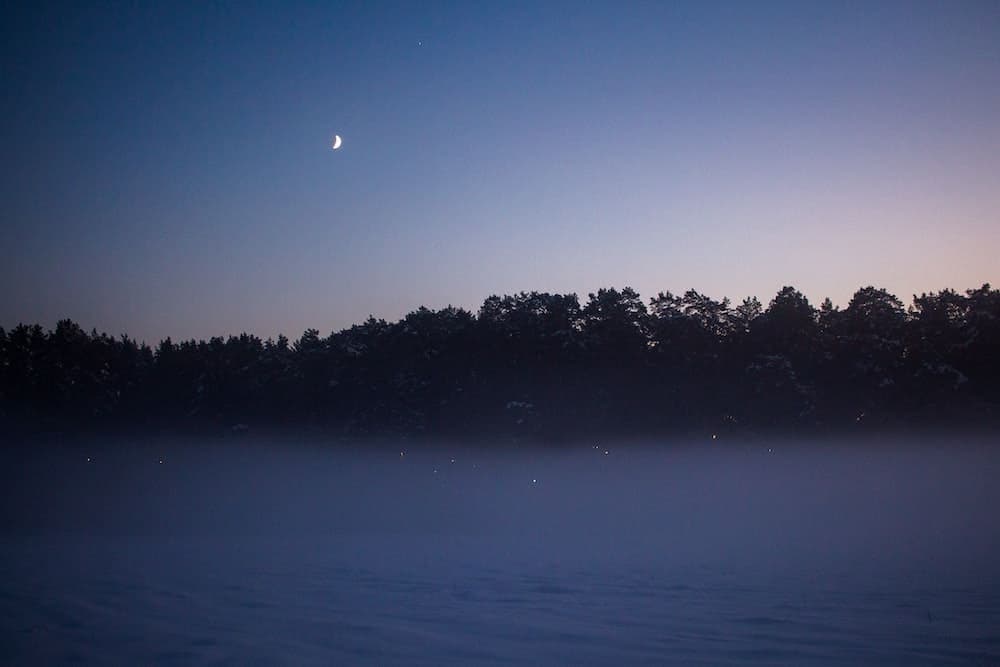 small moon in the background of a lake landscape at night