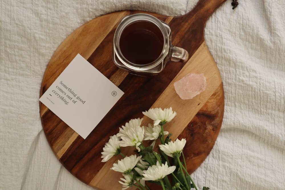 board with coffee, rose quartz crystal, flowers and a note that reads "something good comes out of everything"