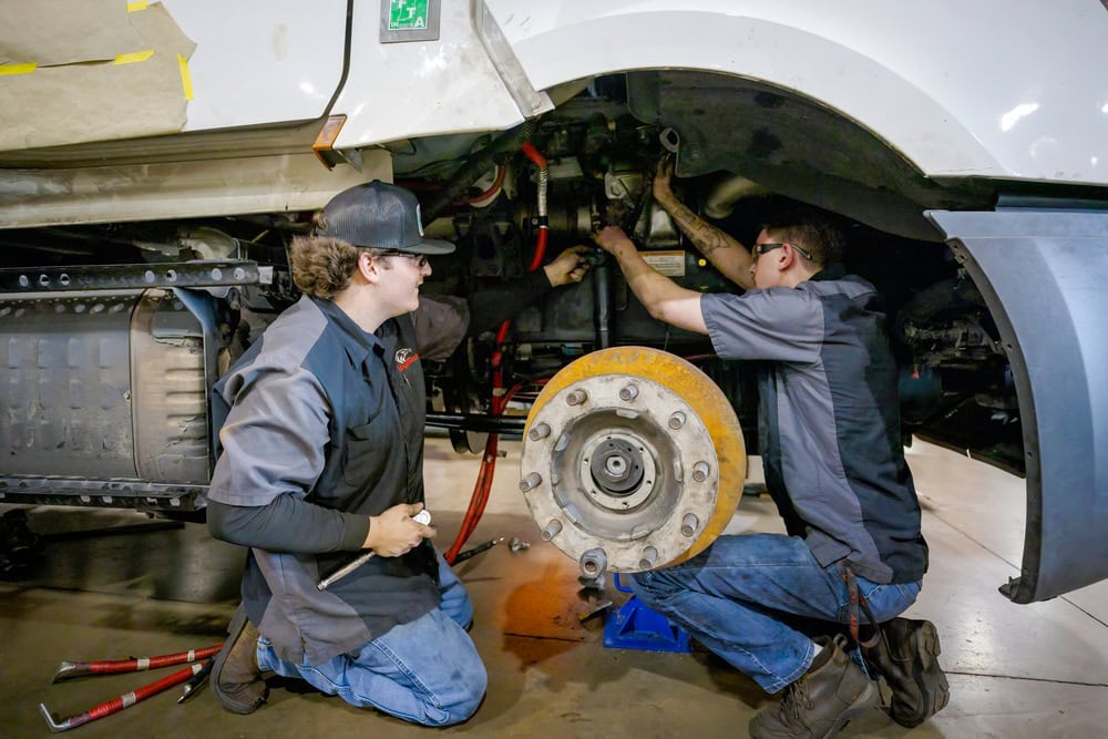 Two students working on the wheel of a semi truck.