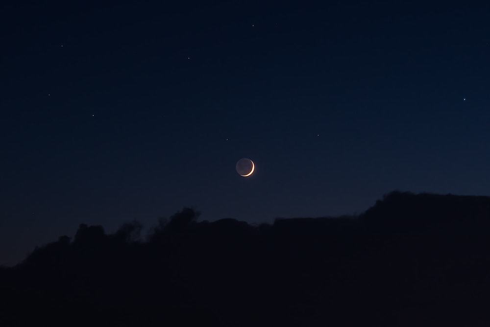 illuminated moon outline on dark blue background with black silhouette of trees