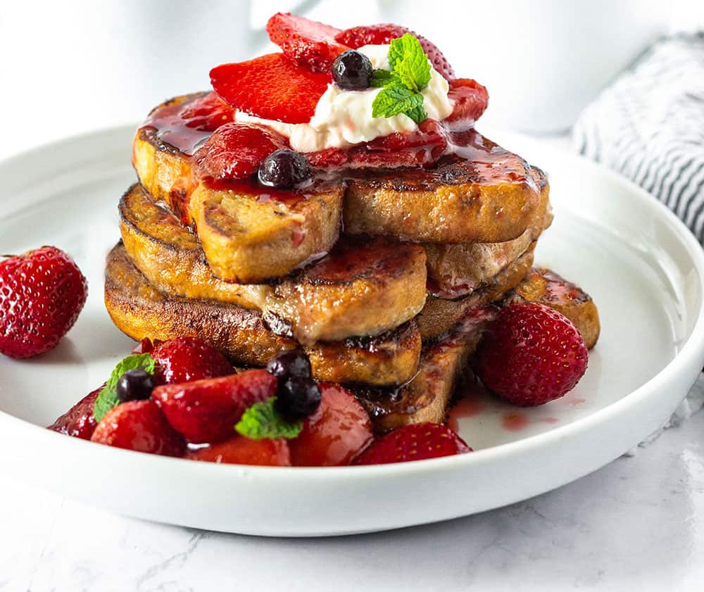 stack of french toast with strawberry sauce and garnishings dripping down onto white plate