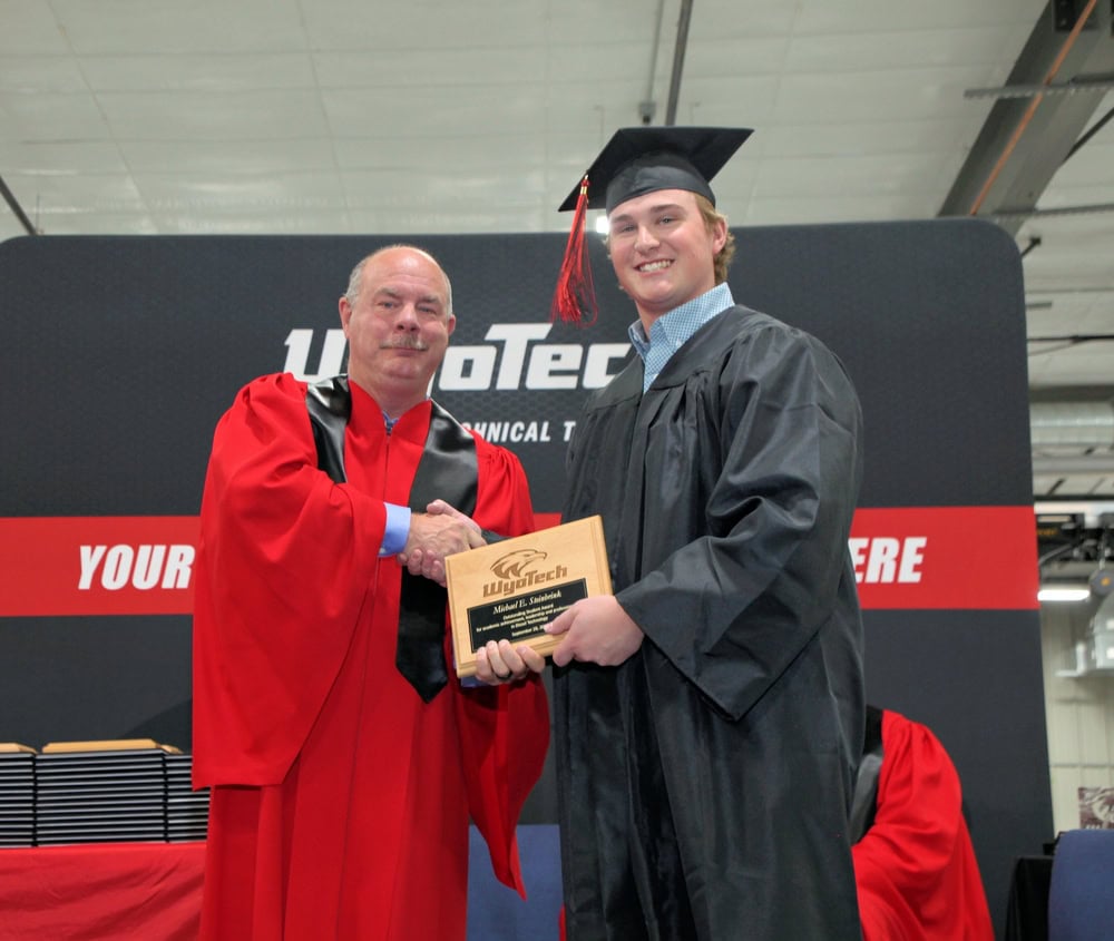 A student shaking the hand of an instructor at a graduation ceremony.