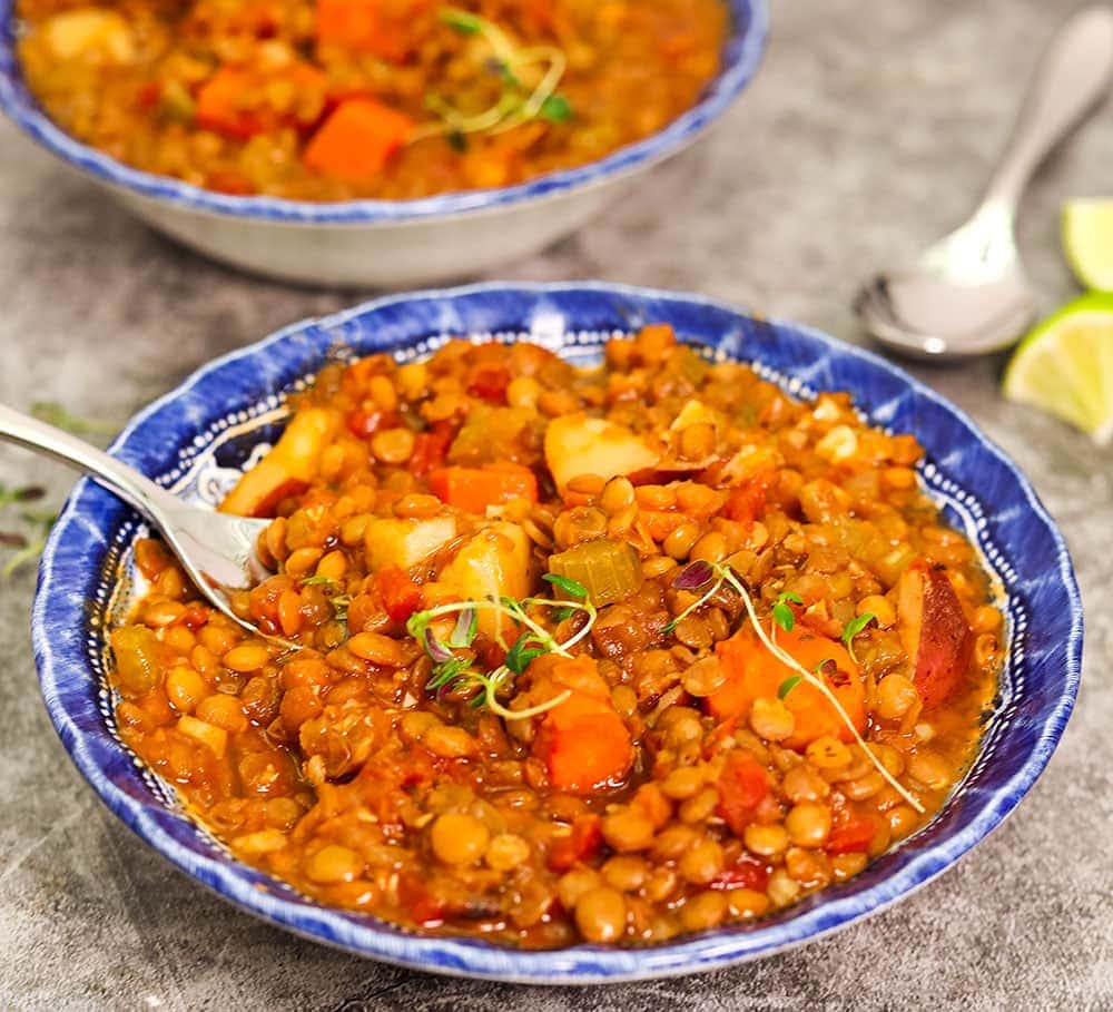 close up lentil stew in two blue bowls with a fork on a grey background