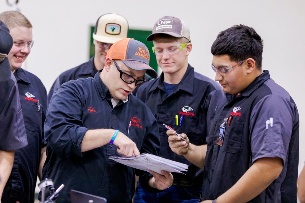 Four WyoTech students listening to an instructor as he points to a paper in his hand.