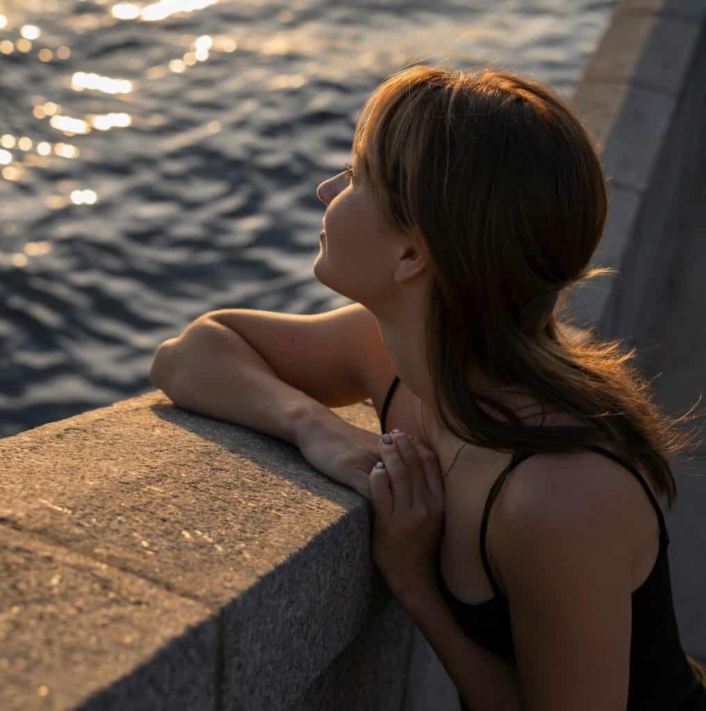 girl romanticising life on solo date, smiling looking out over a wall to the ocean
