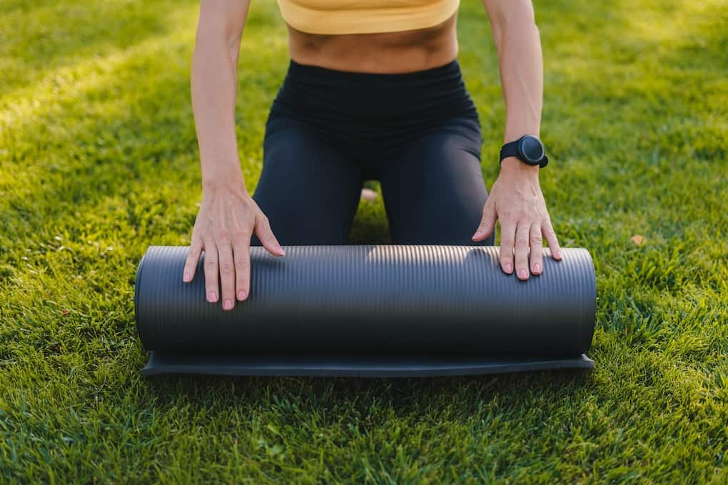 woman rolling out yoga mat on the grass