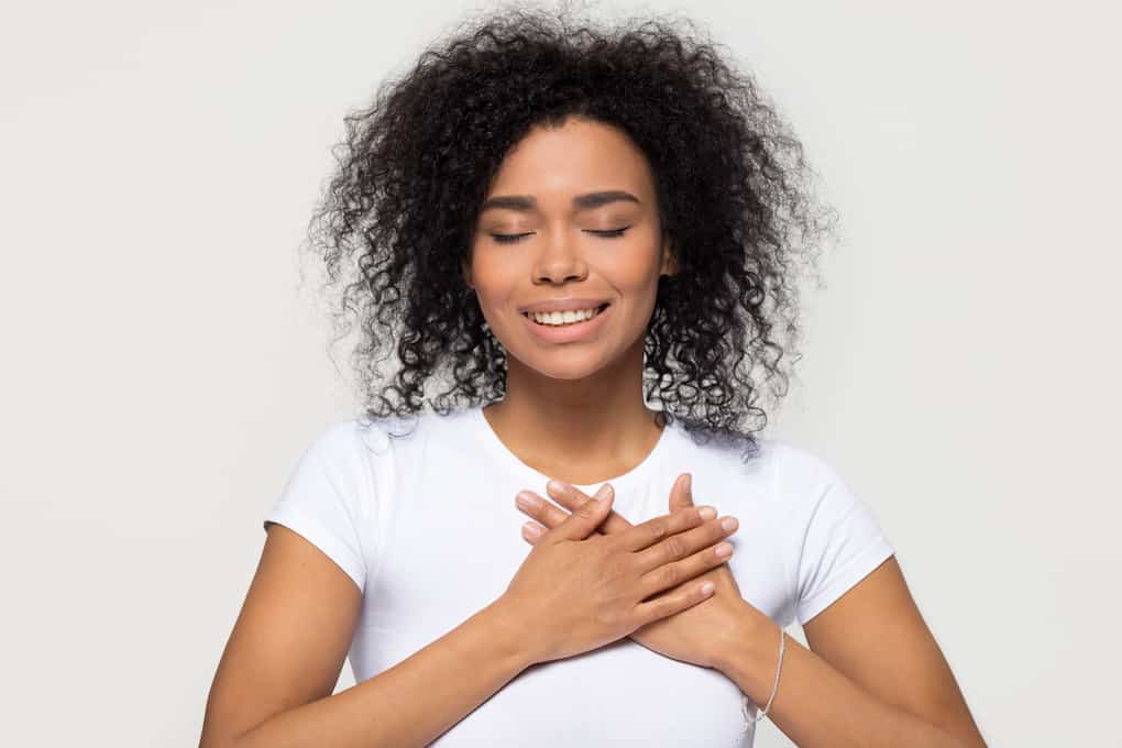 woman with hands on heart, eyes closed and smiling looking grateful and relieved