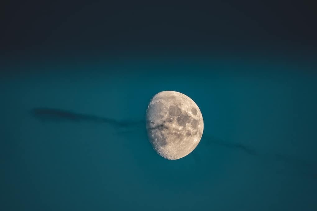 A beautiful shot of a waxing gibbous moon in a dark blue sky with a wispy cloud