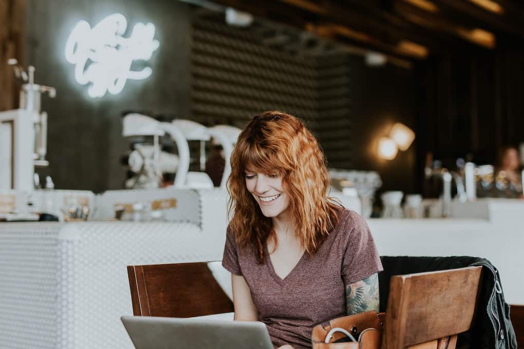 woman with tattoos smiling at laptop doing solo work in a cafe