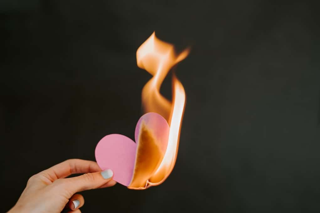 hand holding pink paper heart set on fire