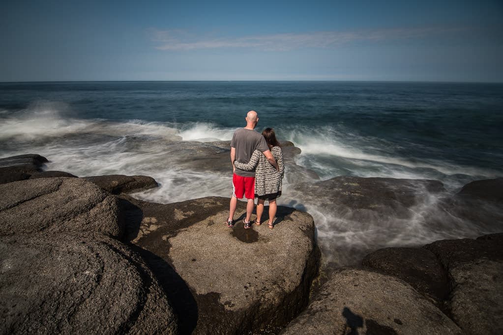 Brooke and Buddy standing side by side watching waves crash in front of them at Point Riche Lighthouse