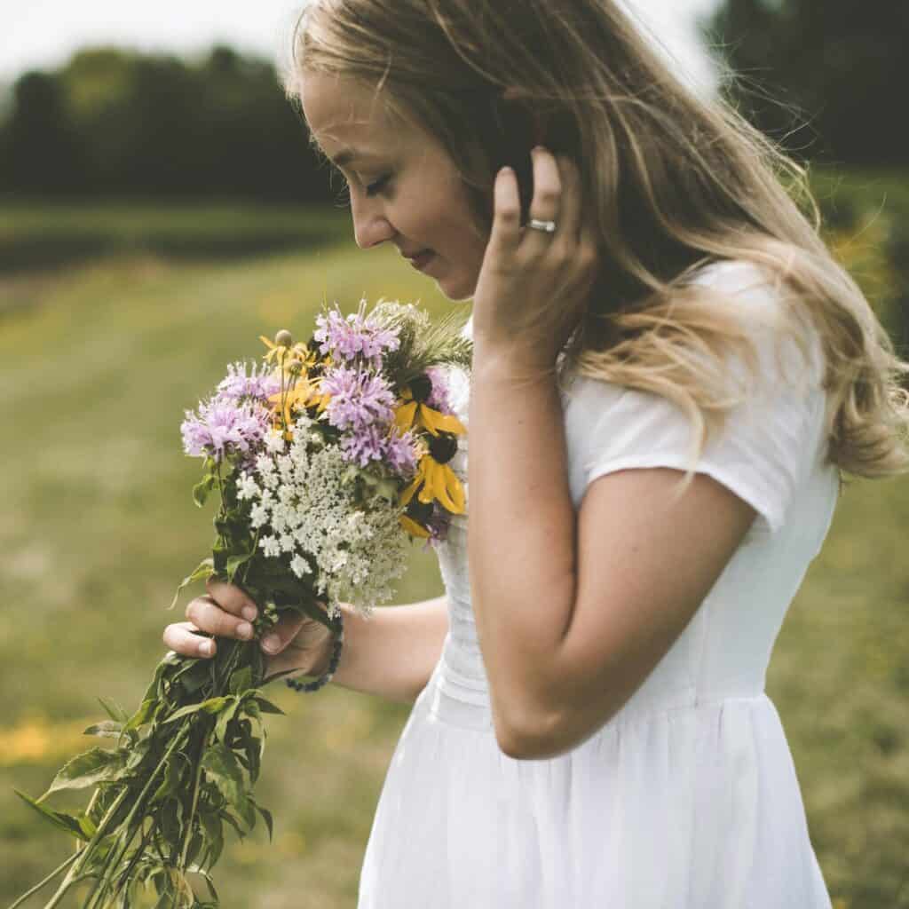 feminine woman in white flowy dress in a field smelling a bunch of hand picked flowers, soft girl aesthetic