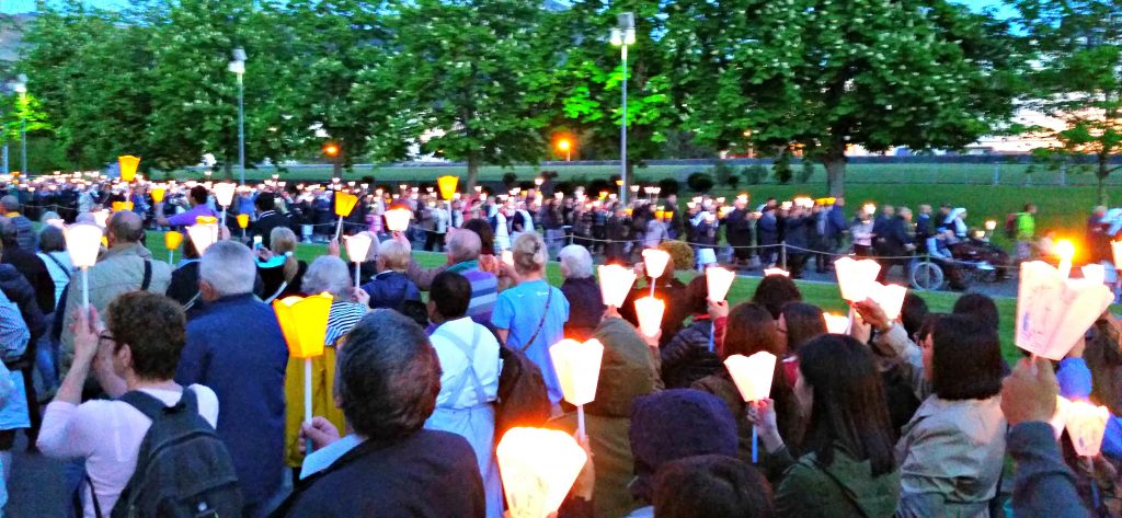 Candlelight processional of people walk along a boulevard in Lourdes, France.