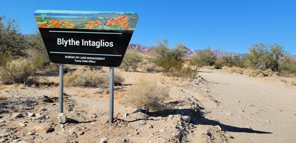 BLM sign in the desert reads "Blythe Intaglios" near dusty gravel road