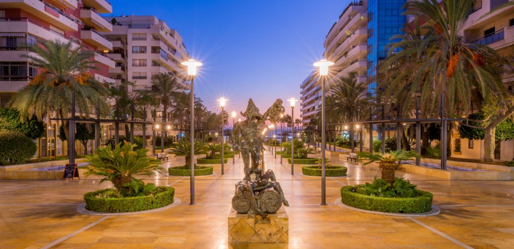 paved avenue with white street illuminating a modernistic statue