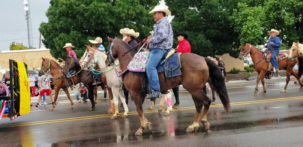 8 cowboys in straw hats ride their well-trimmed horses along street in Hatch Chile Festival parade