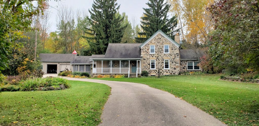 large farmhouse made of stone and poured cement sit on wide green lawn on the WI Way, with pine and oaks rising behind