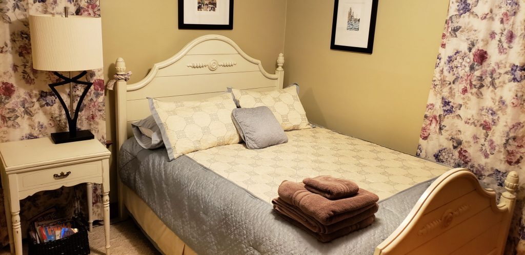 queen bed with lamp on white French provincial night stand - towels are stached on bed waiting to welcome the next guest to this Elkhart Lake lodging
