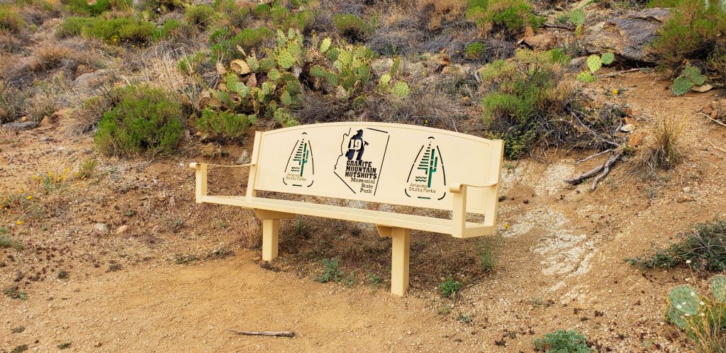 benchh in the desert with prickly pear catus behind. The number 19 is cut out of the metal chair back at Granite Mountain Hotshots Memorial Sate Park
