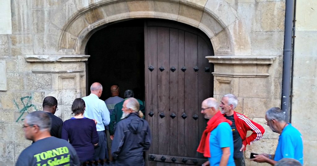 Groups of pilgrims enter the double door of the chapel at Monasterio de Benedictinas Santa María de Carbajal León. A stone arch is over the doors.