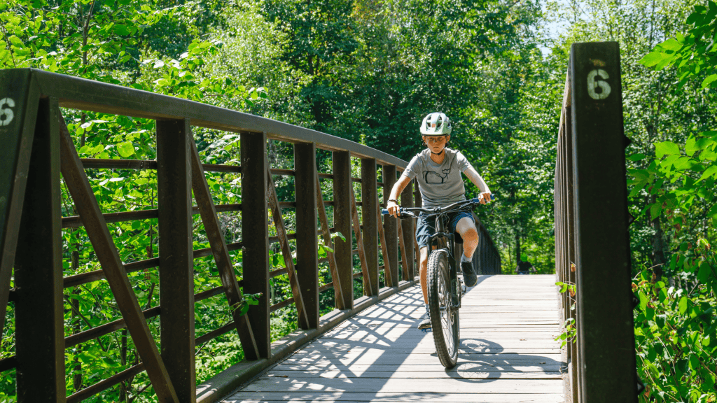 A young rider mountain biking through a forested trail in Stowe, Vermont (Photo By Maura Wayman Photography)