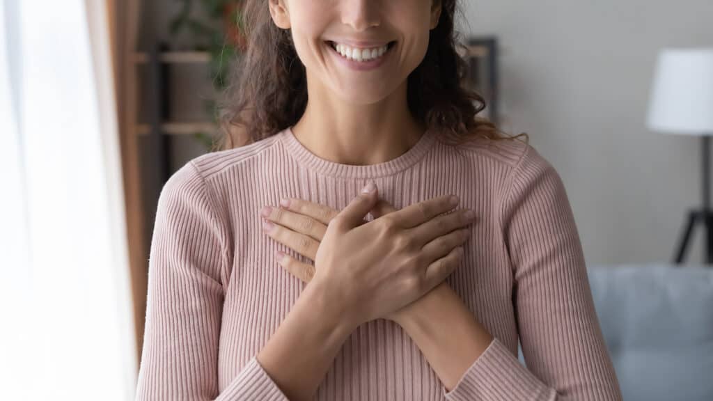 close up of woman smiling with hands on heart feeling grateful