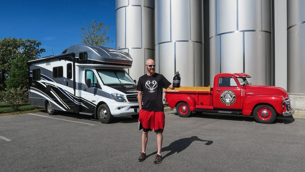 Buddy standing in front of our RV holding a growler full of cider at Woodchuck Cidery in vermont