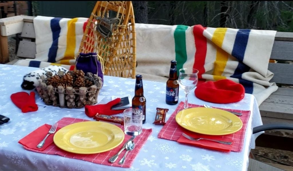 Outdoor table set with snowflake table cloth, red napkins with Canadian flags, Labatt's beer, Hudson Bay blanket, snowshoes and Croen Royal whiskey in purple flannel bag