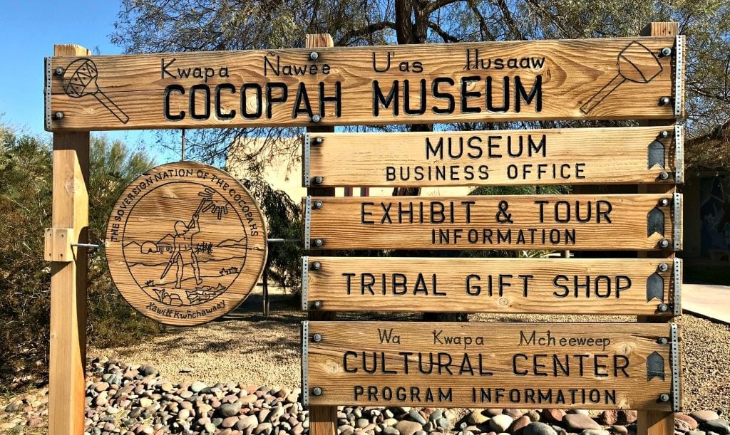 Rustic wooden sign with letters burned into wood. Reading in part "Cocopah Museum"