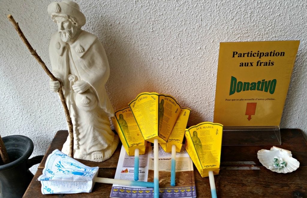 statue of st james, candles with paper cone to catch dripping wax and a donation box on wood table