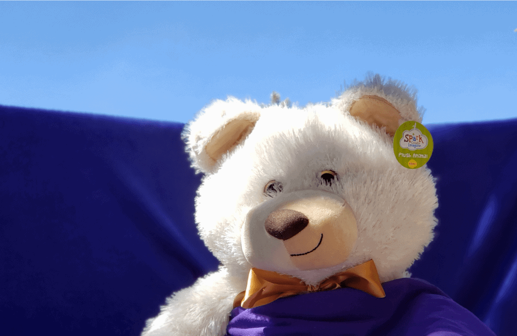 Plush stuffed polar bear toy sits in "field of purple flowers" which is really a purple blanket