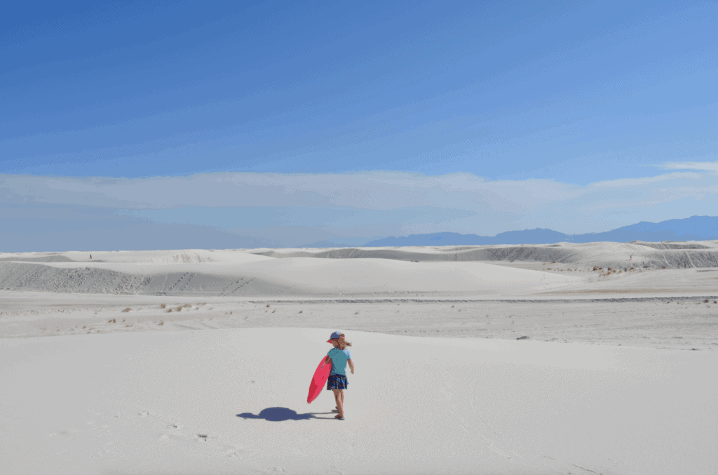 girl holding pink sled in white sand