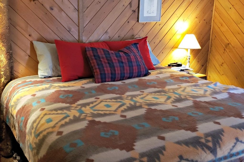 Bedroom with cedar wood walls - bed has Native design bedspread - pillow with red plaid flannel