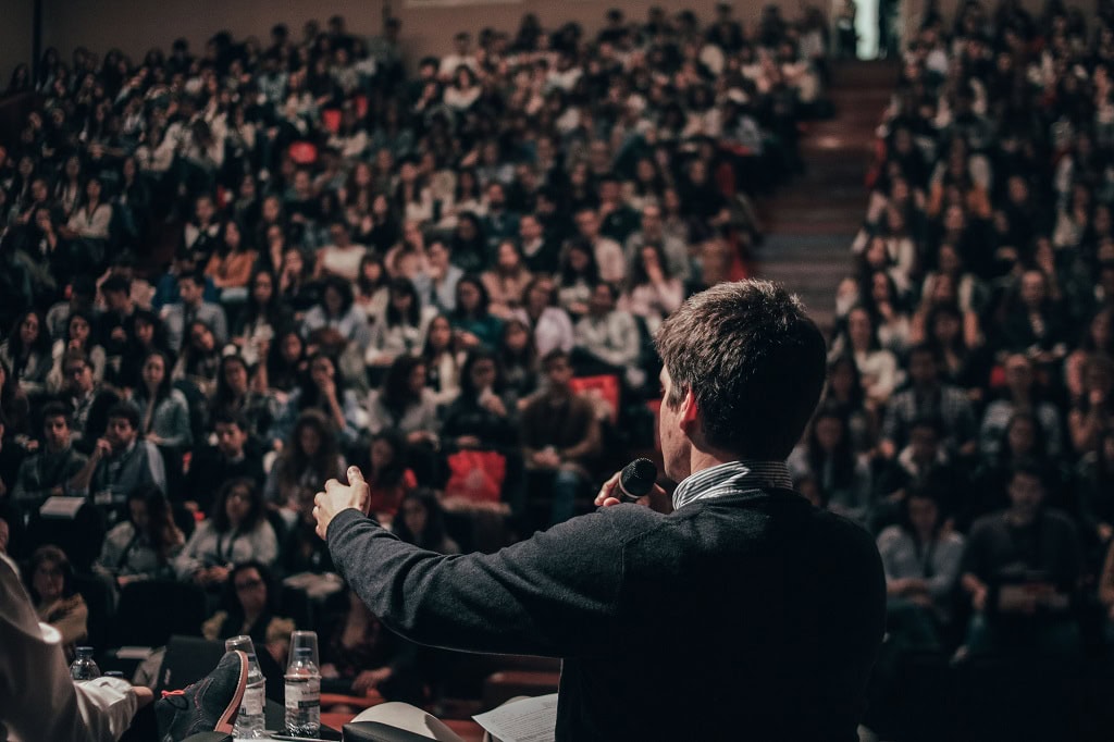 A college student speaks before a packed auditorium.