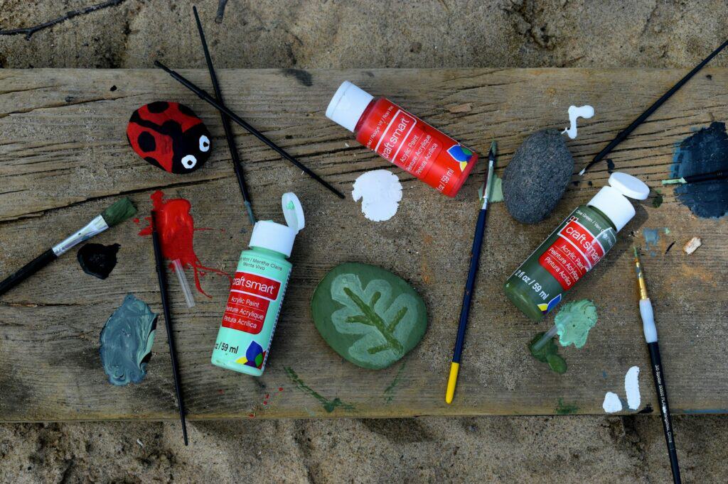 Paints, brushes, and a ladybug rock representing cute painting ideas on rocks