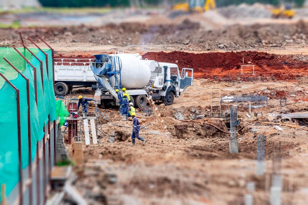 Workers guide activity around a white concrete mixer truck in a muddy construction foundation area.