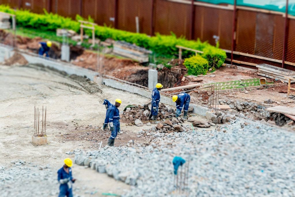 Construction workers in blue uniforms and yellow helmets clear rubble from a work area