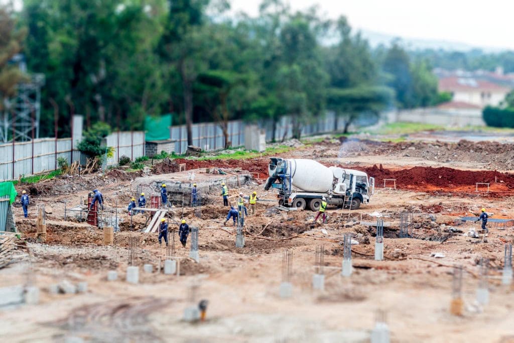 A wide view of a construction site with workers, foundation columns, and a cement mixer