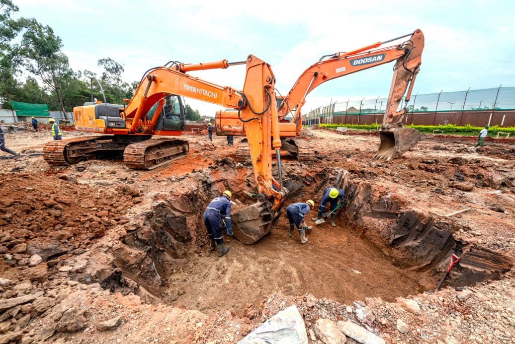 Two orange excavators work beside a deep foundation pit with construction workers
