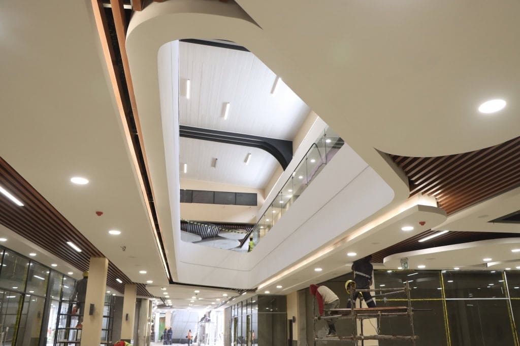 Workers carry out finishing work in a mall corridor with a large atrium and curved ceiling.
