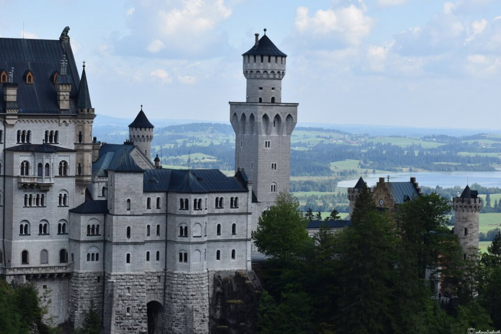 exterior facade of Neuschwanstein castle with arched windows, turrets and balcony in the background of green area and lake